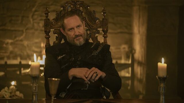 alt="Bertie Carvel as Prince Baelor “Breakspear” Targaryen seated on a throne in front of a fireplace inside a stone hall in A Knight of the Seven Kingdoms."