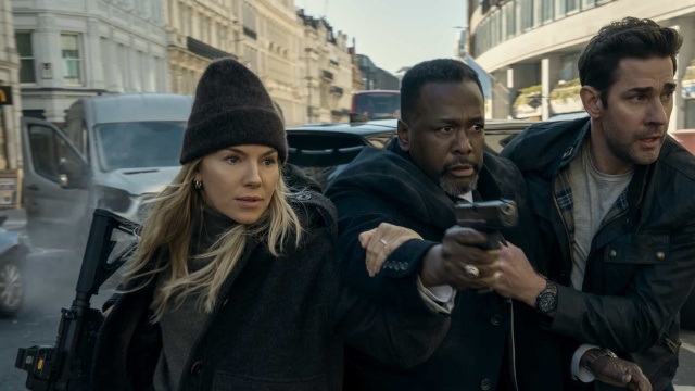 Sienna Miller as Emma Marlowe running with a gun in her hand with James and Jack