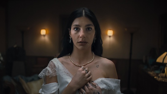 alt="Woman looking scared wearing a white wedding dress and holding her necklace"