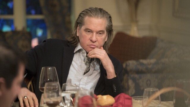 alt="Val Kilmer seated at a dinner table looking serious in The Birthday Cake, 2021 crime drama"